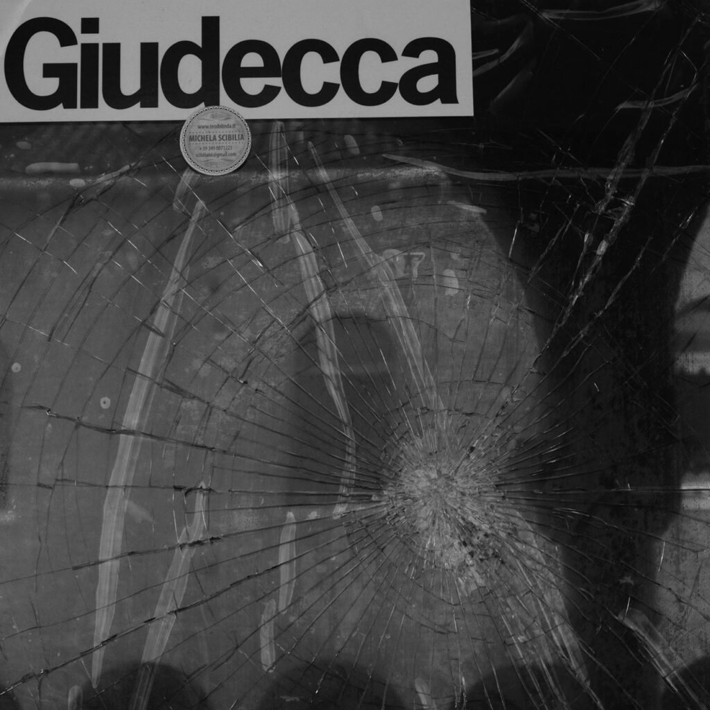 foto di un vetro rotto con scritto Giudecca. Link alla galleria fotografica.